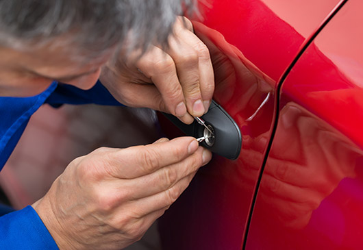 A man fixing the door handle of a red car.